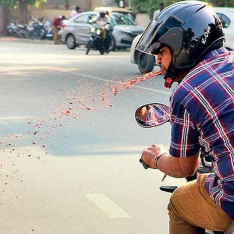 indian man spitting gutka on street while riding on bike